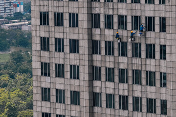 Window cleaners hanging from ropes are diligently washing the glass facade of a towering skyscraper, ensuring a spotless urban view. Bangkok, Thailand