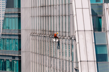 High-rise window cleaner performing maintenance on a modern skyscraper, ensuring sparkling clean windows for a pristine appearance. Bangkok, Thailand