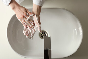 Woman washing hands with cleansing foam near sink in bathroom, top view