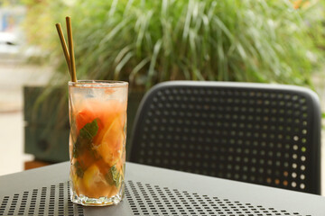 Glass of tasty refreshing drink and straws on table in outdoor cafe