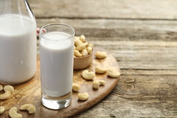 Fresh cashew milk in glass, bottle and nuts on wooden table, closeup. Space for text