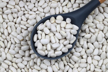 White Beans in a wooden spoon close-up on a wooden background. Vegetarian food.