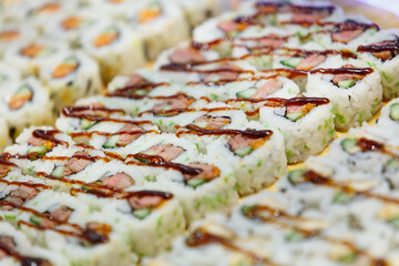 Close-up of numerous sushi rolls, likely teriyaki.  Rows of rice rolls with visible fillings and...