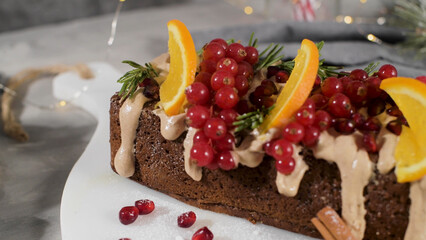 A festive loaf cake decorated with orange slices, red currants, and rosemary sprigs, drizzled with a creamy frosting and sprinkled with cinnamon