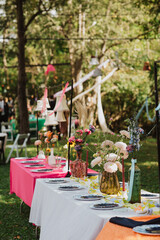 Colorful Garden Party Tablescape with Floral Arrangements, Vibrant Tablecloths, Hanging Lamps, and Rustic Outdoor Setting for a Perfect Celebration
