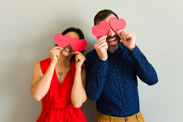 Smiling couple holding red paper hearts over their eyes, celebrating valentine's day and sharing their love