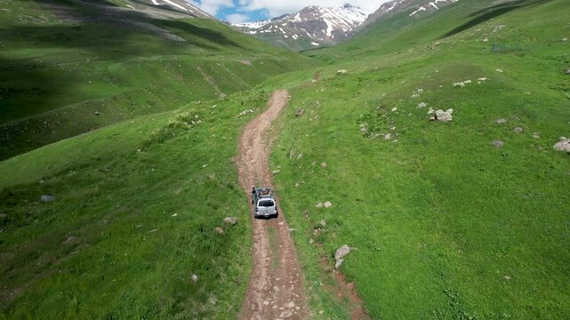 Drone follows an SUV going up the slope of Mount Aragats along Gagharot river on sunny summer day. Armenia.