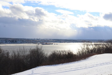 Winter landscape in a park in Quebec city with trees a sunny sky and a large river. Winter and december calendar. A background with snow and an horizon. The St-Laurent river in winter.