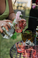 Pouring Drinks at an Outdoor Garden Party with Vibrant Amber and Pink Glassware, Fresh Floral Decor, and Stylish Summer Vibes