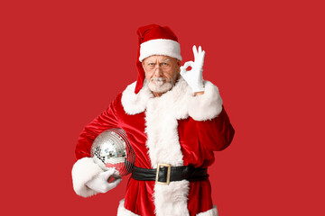 Displeased Santa Claus in glasses with disco ball showing OK gesture on red background