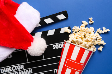 Movie clapper with Santa hat and bucket of popcorn on blue background