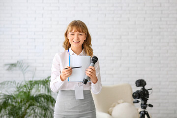 Young happy female reporter with microphone pointing at notebook in office