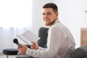 Male reporter with microphone and notebook sitting in armchair at studio