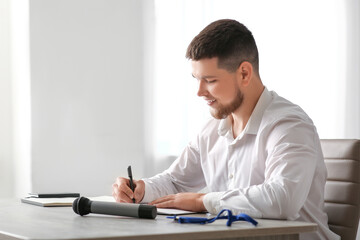 Male reporter with microphone and notebook sitting at table in office