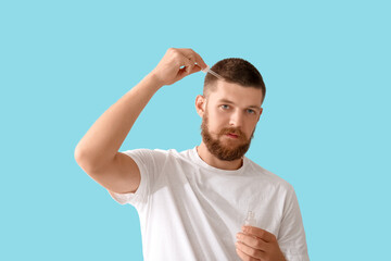 Young man using serum for hair growth on blue background. Hair loss concept