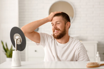 Happy young man with hair loss problem near mirror at home