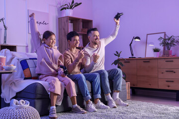 Happy father with his children playing video game on sofa at home in evening
