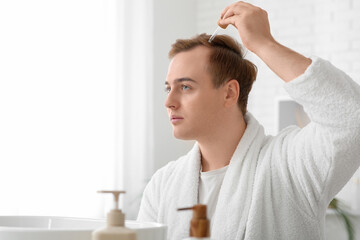 Young redhead man applying serum for hair growth in bathroom, closeup