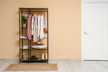 Rack with clothes and shoes near beige wall