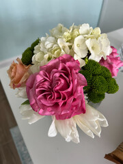 A vibrant floral arrangement featuring pink roses, white hydrangeas, green button poms, and soft peach blooms in a delicate composition.