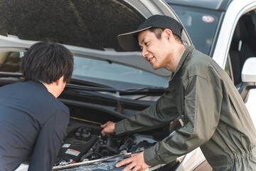自動車のエンジンルームでドライバーに説明する整備士の男性スタッフ
