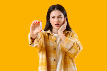 Young woman with ear drops on yellow background