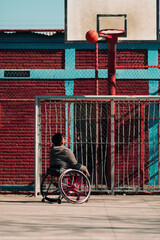 Obraz premium Young Latino athlete in wheelchair, training, playing and shooting basketball in a city park outdoors