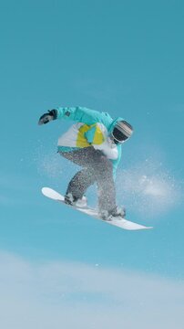 SLOW MOTION, TIME WARP: Male snowboarder flies through the air and does a rotating grab trick while shredding slopes in the sunny Slovenian mountains. Action shot of a snowboarding pro doing tricks.