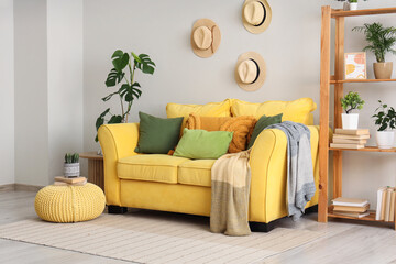 Obraz premium Yellow sofa and pouf with books and cactus in interior of living room
