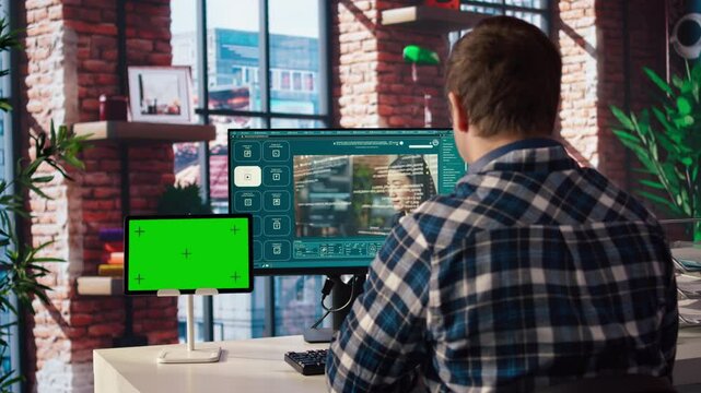 Man in home office uses AI program turning text prompt into videos next to isolated screen tablet. Person using text to video generative models on computer and chroma key device, camera A