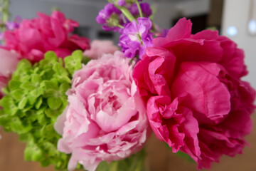 A vibrant floral arrangement featuring a bold magenta peony, soft pink blossoms, lush green hydrangeas, and delicate purple flowers, showcasing natural beauty against a softly blurred background.