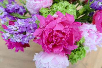 Bright pink peonies, purple blossoms, and lush green accents arranged in a vibrant spring bouquet,...