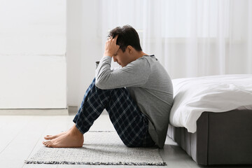 Depressed young man sitting on carpet in bedroom