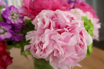 Soft pink peony petals take center stage in this floral arrangement, accompanied by purple blooms, green hydrangeas, and hints of vibrant red, creating a fresh and elegant bouquet.