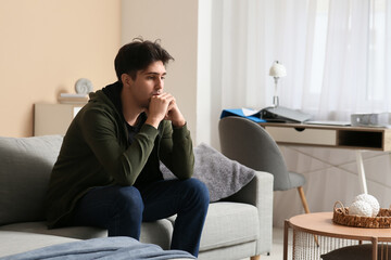 Fototapeta premium Young man experiencing mental health challenges, depression, and anxiety while sitting alone on a sofa at home