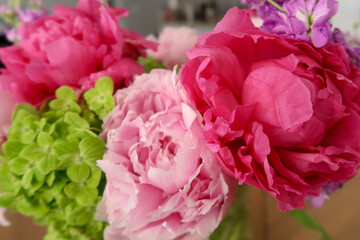 A vibrant bouquet showcasing bold magenta peonies, soft pink petals, and fresh green hydrangeas, arranged in a natural, delicate composition with blurred background details indoors.