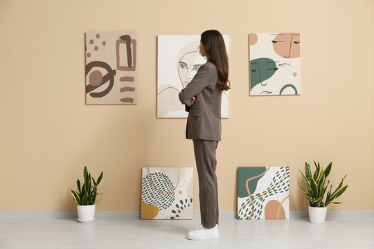 Young woman looking at paintings on beige wall in art gallery