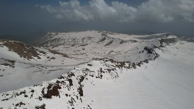Forward reveal aerial shot of slope of Mount Aragats covered with snow on sunny spring day. Armenia.