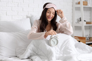 Awake young woman with sleeping mask and alarm clock in bedroom