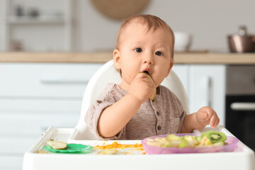 Cute little baby eating pear in high chair at home