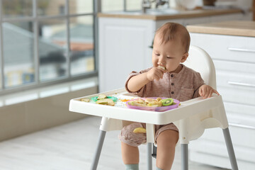 Cute little baby eating fruit in high chair at home