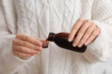Woman pouring cough syrup from bottle into measuring cup on white background, closeup