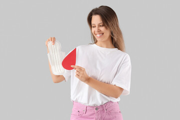 Young woman with menstrual pad and paper blood drop on light background