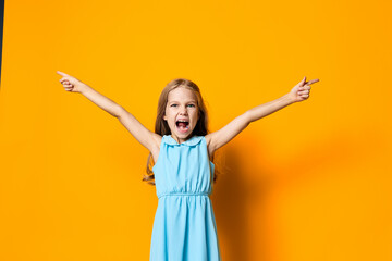 Joyful little girl in blue dress standing with arms outstretched against vibrant orange background