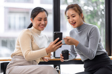 Two asian Female friends drinking coffee and using mobile phones while sitting at cafe
