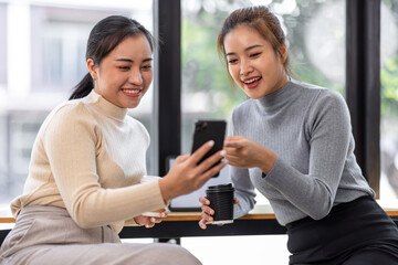 Two asian Female friends drinking coffee and using mobile phones while sitting at cafe
