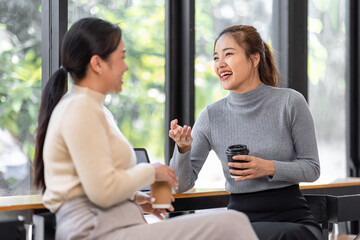 Two asian Female friends drinking coffee and using mobile phones while sitting at cafe
