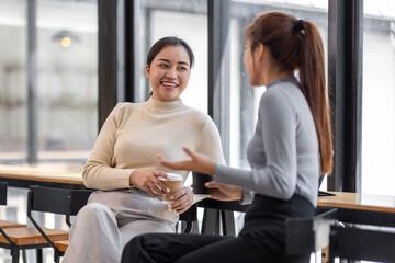 Two asian Female friends drinking coffee and using mobile phones while sitting at cafe
