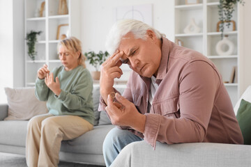 Sad mature man with wedding ring and his wife sitting at home. Divorce concept