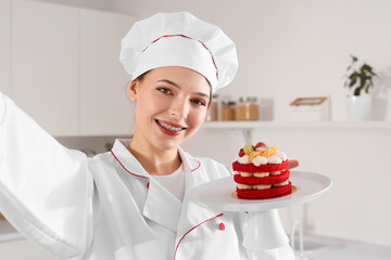 Female confectioner with tasty cake taking selfie in kitchen, closeup
